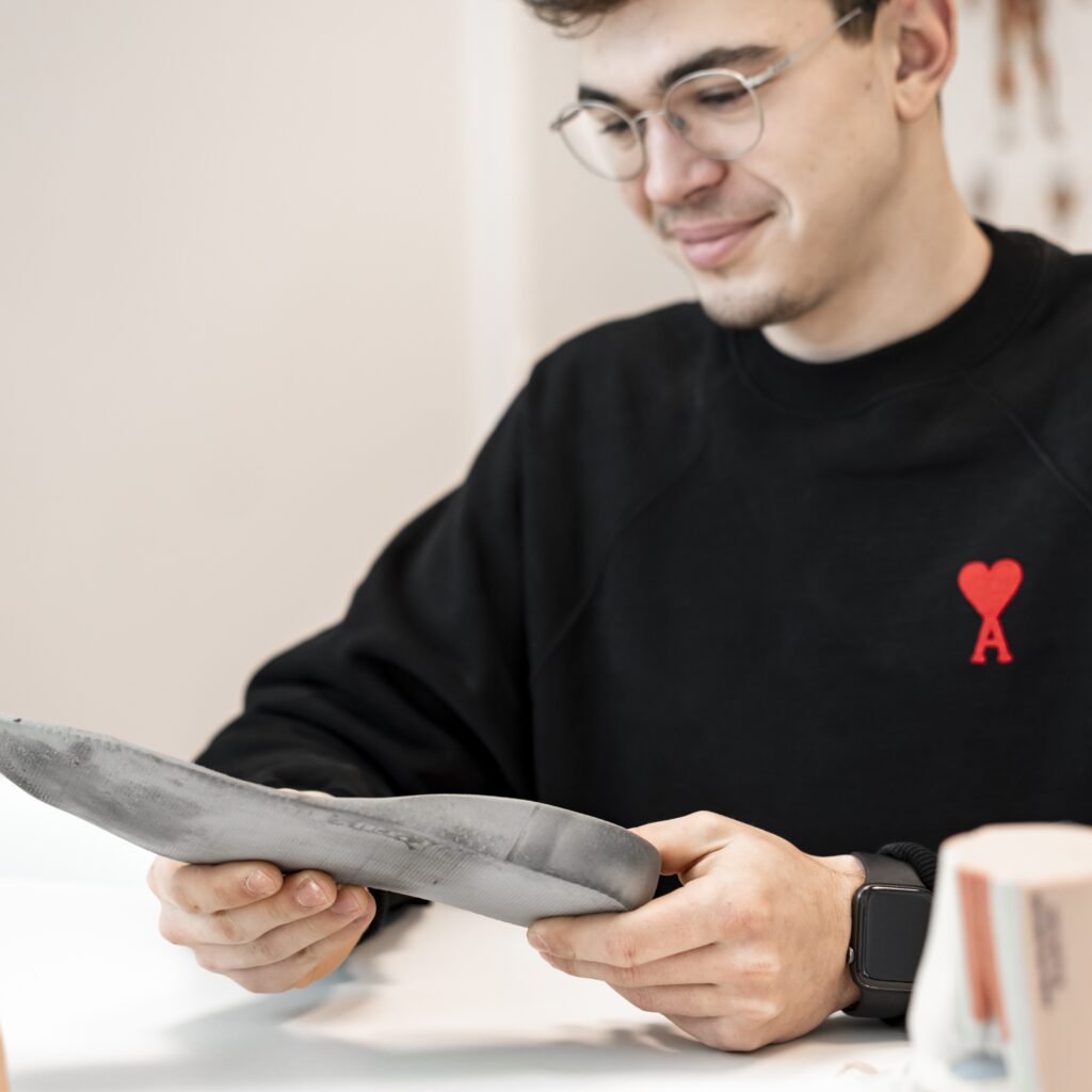 Man met witte bril houdt een podologische zool vast voor voetondersteuning en comfort.