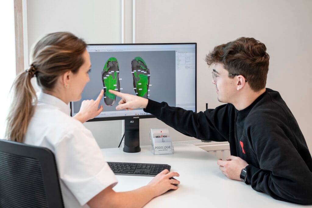 Orthopedische steunzolen of podologische zolen? 4 Margaux Verstraete bespreekt de 3D-voetscan met een patiënt aan de computer