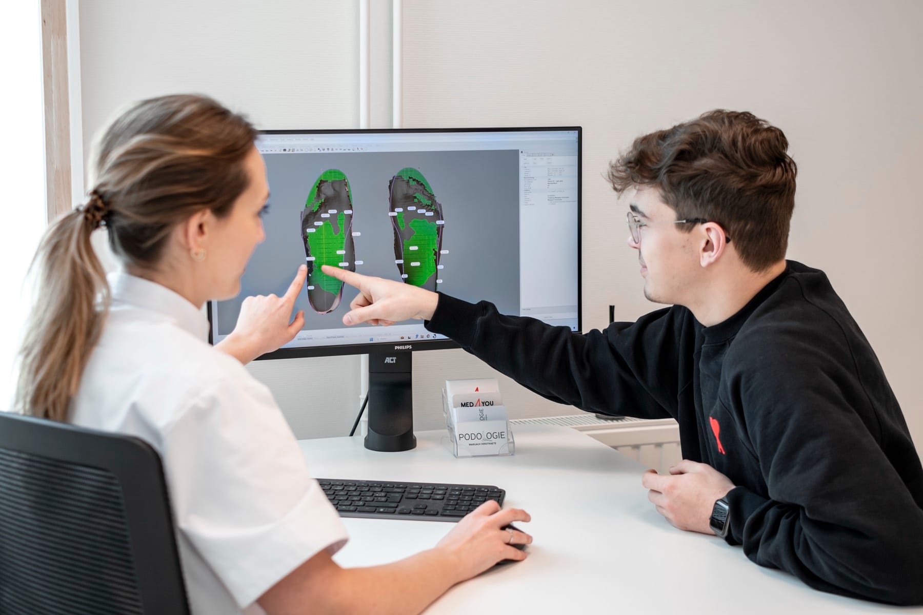Margaux Verstraete bespreekt de 3D-voetscan met een patiënt aan de computer