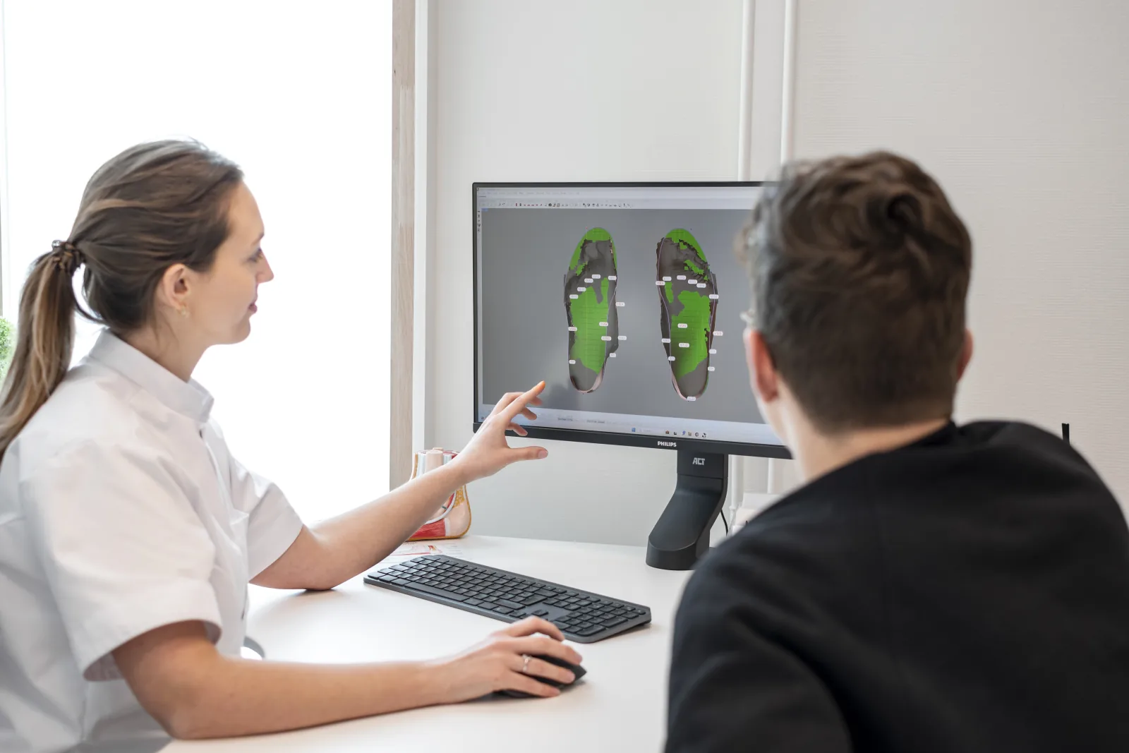Podologie voor bedrijven 4 Margaux Verstraete wijst op een beeldscherm naar de 3D-voetscan van een patiënt